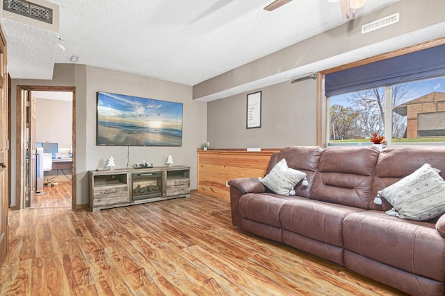 living room with a textured ceiling, light hardwood / wood-style flooring, and ceiling fan