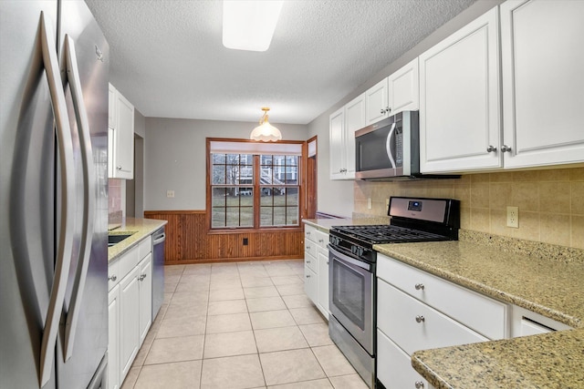 kitchen with light stone countertops, appliances with stainless steel finishes, wooden walls, and white cabinetry