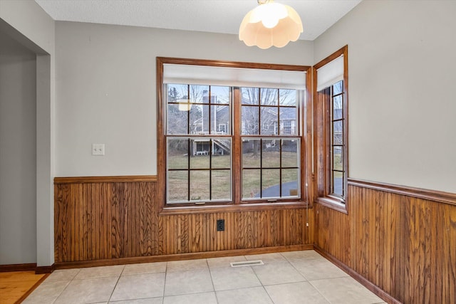 empty room with ceiling fan, wood walls, and light tile patterned floors