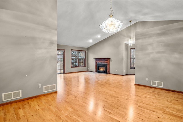 unfurnished living room featuring a brick fireplace, light wood-type flooring, an inviting chandelier, and vaulted ceiling