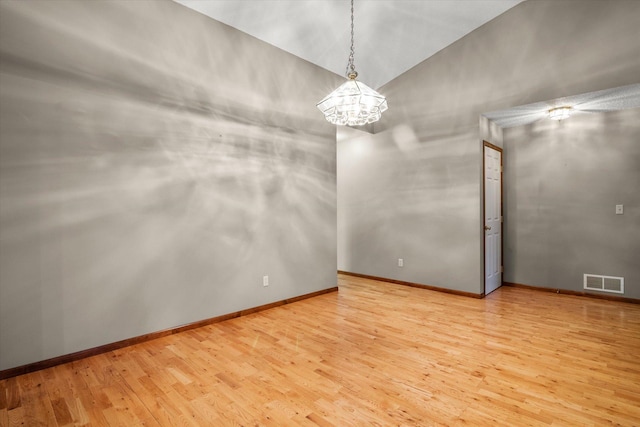 spare room featuring light wood-type flooring, vaulted ceiling, and a chandelier