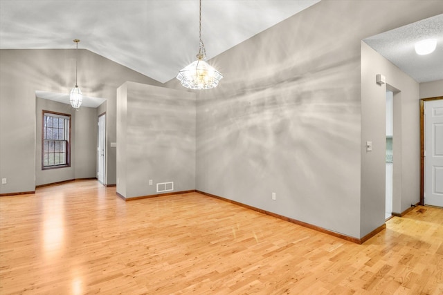 empty room with a notable chandelier, light hardwood / wood-style floors, and lofted ceiling