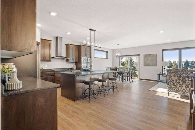 kitchen featuring a kitchen bar, wall chimney exhaust hood, pendant lighting, stainless steel appliances, and light hardwood / wood-style floors