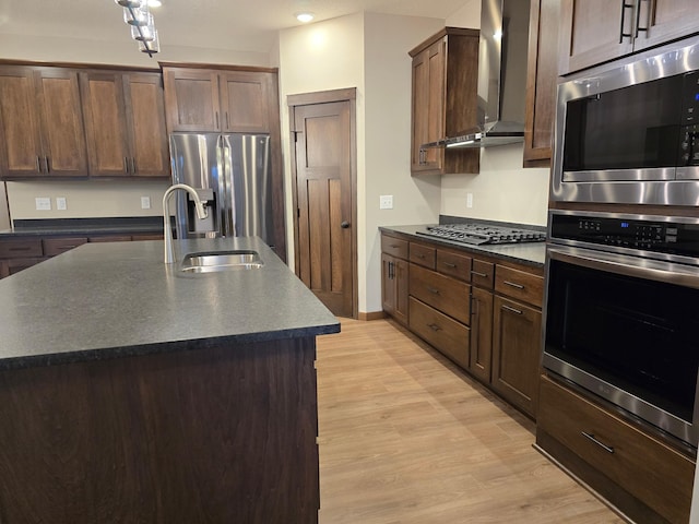 kitchen featuring sink, appliances with stainless steel finishes, wall chimney exhaust hood, and a center island with sink