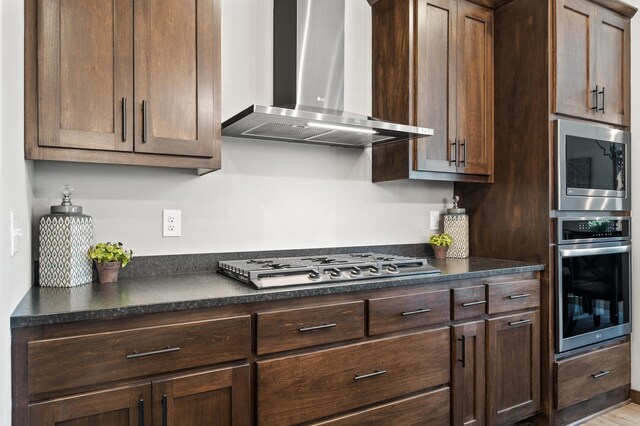 kitchen featuring appliances with stainless steel finishes, wall chimney exhaust hood, and dark brown cabinets