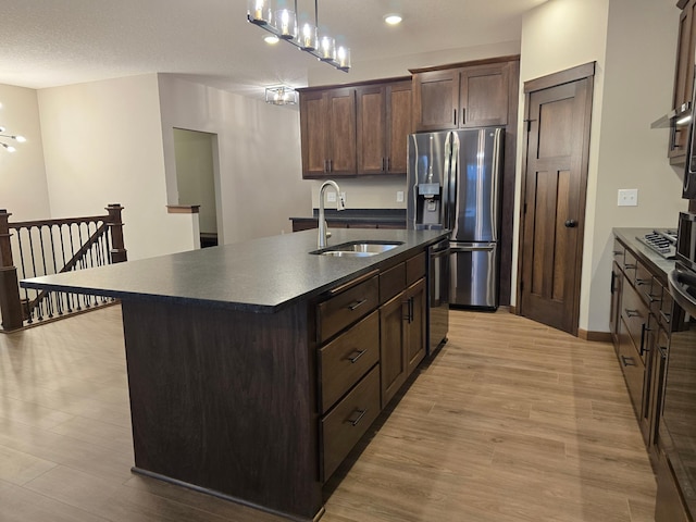 kitchen with sink, dark brown cabinets, stainless steel appliances, an island with sink, and light wood-type flooring