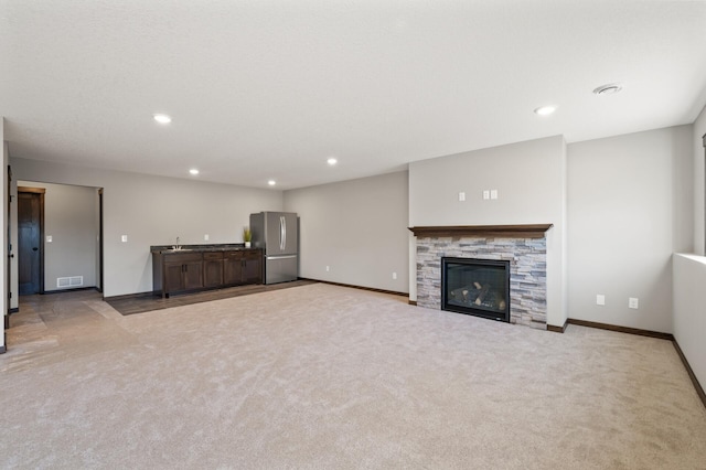 unfurnished living room featuring sink, a fireplace, and light colored carpet