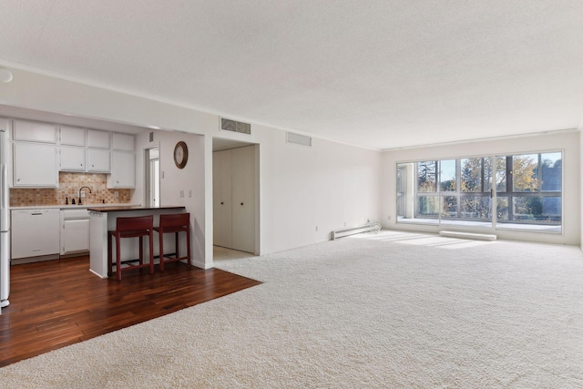 unfurnished living room featuring a textured ceiling, dark hardwood / wood-style floors, a baseboard radiator, and sink