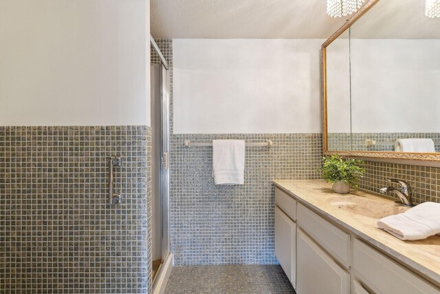 bathroom with a shower with door, vanity, tile walls, and a textured ceiling