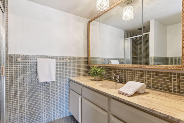 bathroom with a shower with door, vanity, and tile walls