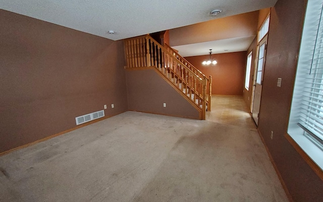 unfurnished living room with an inviting chandelier, a textured ceiling, and light carpet