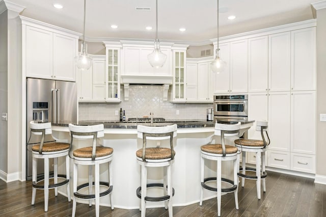 kitchen featuring high quality fridge, a center island with sink, white cabinets, and decorative light fixtures