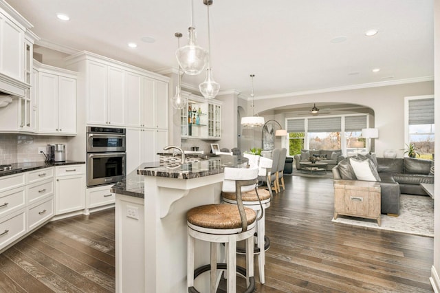 kitchen featuring a breakfast bar, ceiling fan, dark wood-type flooring, and an island with sink