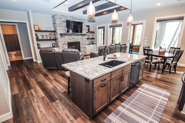 kitchen with dishwasher, dark wood-type flooring, sink, light stone countertops, and an island with sink