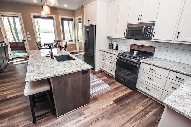 kitchen featuring pendant lighting, black appliances, sink, an island with sink, and white cabinetry