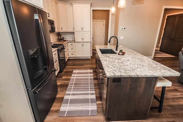 kitchen with white cabinetry, hanging light fixtures, tasteful backsplash, an island with sink, and black appliances