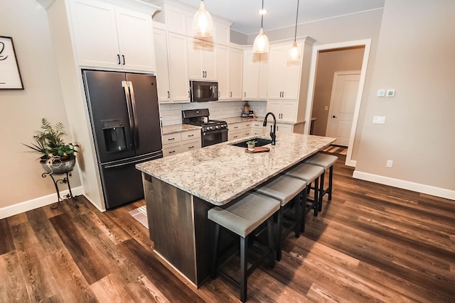 kitchen featuring sink, black appliances, a center island with sink, white cabinets, and hanging light fixtures