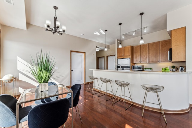 kitchen featuring brown cabinets, dark wood finished floors, hanging light fixtures, appliances with stainless steel finishes, and a peninsula