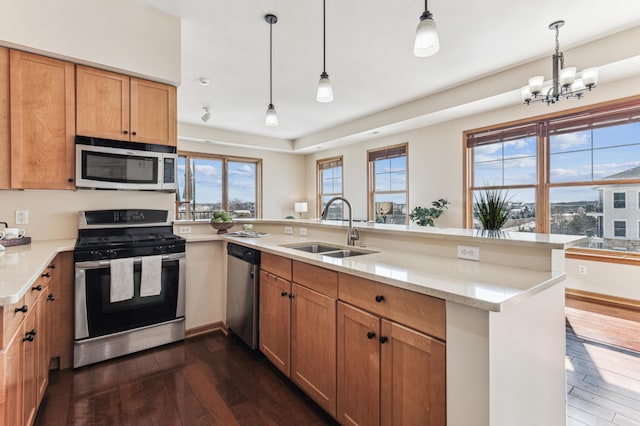 kitchen featuring dark wood-style flooring, stainless steel appliances, hanging light fixtures, a sink, and a peninsula