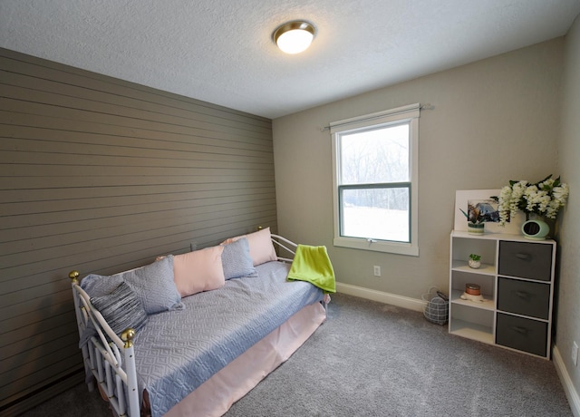 bedroom featuring a textured ceiling, wooden walls, and dark carpet