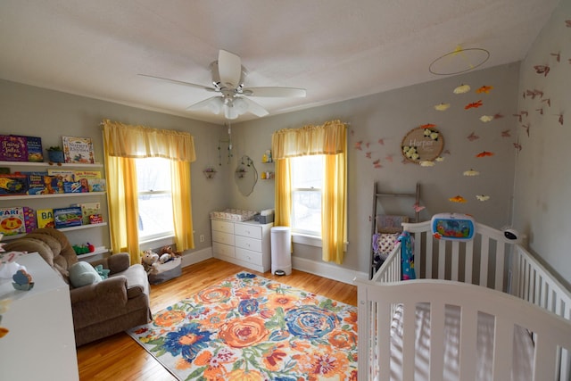 bedroom featuring a crib, multiple windows, light hardwood / wood-style flooring, and ceiling fan