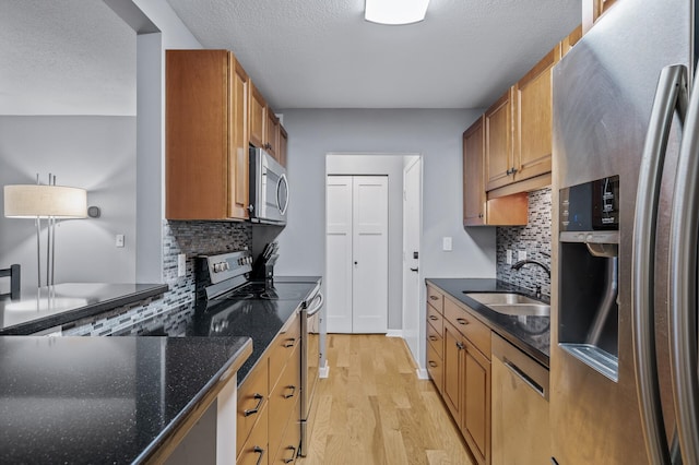 kitchen featuring tasteful backsplash, stainless steel appliances, sink, dark stone countertops, and light hardwood / wood-style floors