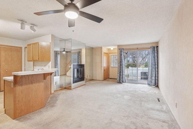 interior space with ceiling fan, kitchen peninsula, pendant lighting, light colored carpet, and a textured ceiling