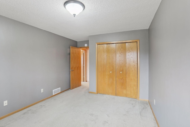 unfurnished bedroom featuring light carpet, a textured ceiling, and a closet