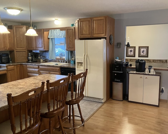 kitchen featuring light wood-type flooring, sink, white refrigerator with ice dispenser, pendant lighting, and dishwasher