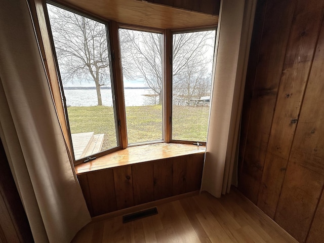 interior space with hardwood / wood-style floors, a water view, and wood walls