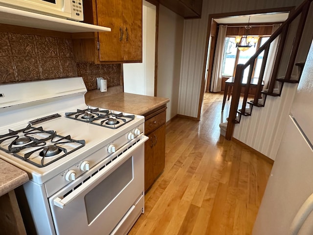 kitchen with an inviting chandelier, pendant lighting, white appliances, light hardwood / wood-style floors, and decorative backsplash