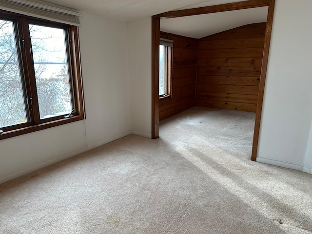 carpeted spare room featuring wood walls and lofted ceiling