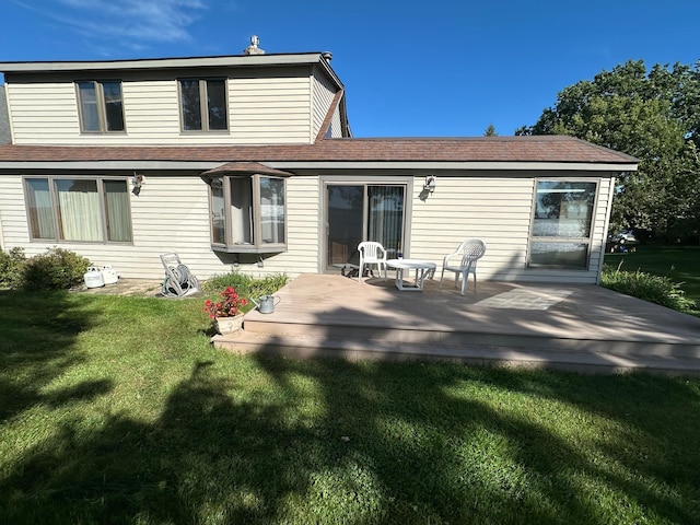 rear view of property with a deck, a yard, and roof with shingles