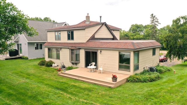 rear view of property featuring a deck, a chimney, a yard, a shingled roof, and cooling unit