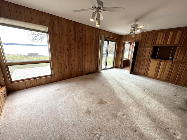 unfurnished living room featuring light carpet, wooden walls, and ceiling fan