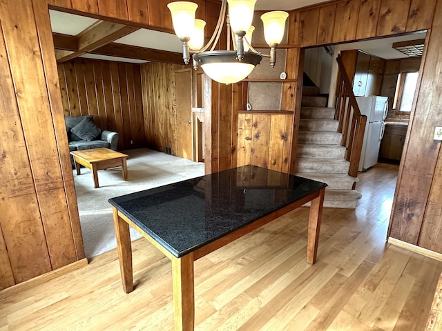 dining space featuring wood walls, light wood-style flooring, a notable chandelier, and stairs