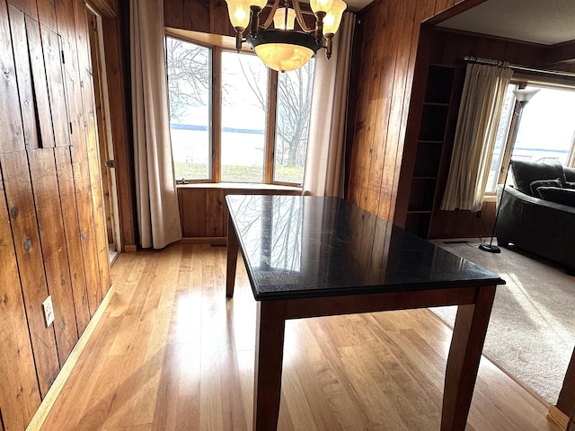 dining space with wooden walls, an inviting chandelier, a wealth of natural light, and light wood-style floors