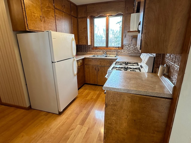 kitchen featuring white appliances, light countertops, brown cabinets, a sink, and light wood-type flooring