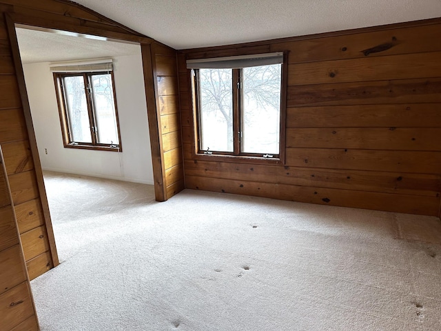 empty room featuring wooden walls, lofted ceiling, light colored carpet, and a textured ceiling