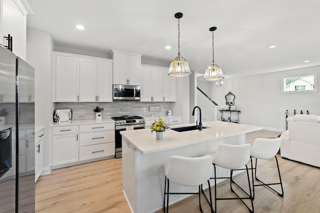 kitchen featuring white cabinets, sink, light wood-type flooring, an island with sink, and stainless steel appliances