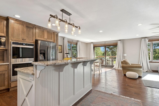 kitchen with stainless steel appliances, light stone counters, a kitchen breakfast bar, a healthy amount of sunlight, and a kitchen island