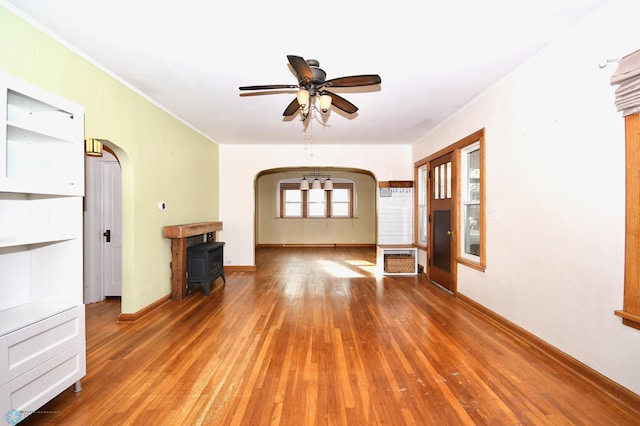 interior space with hardwood / wood-style floors, a wood stove, ceiling fan, and ornamental molding