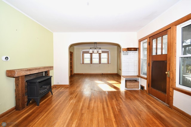 unfurnished living room featuring a wood stove, crown molding, a notable chandelier, and hardwood / wood-style flooring