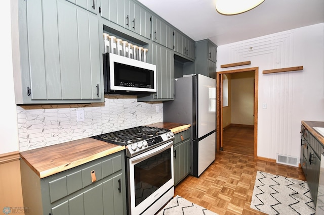 kitchen featuring decorative backsplash, wood counters, stainless steel appliances, and light parquet flooring