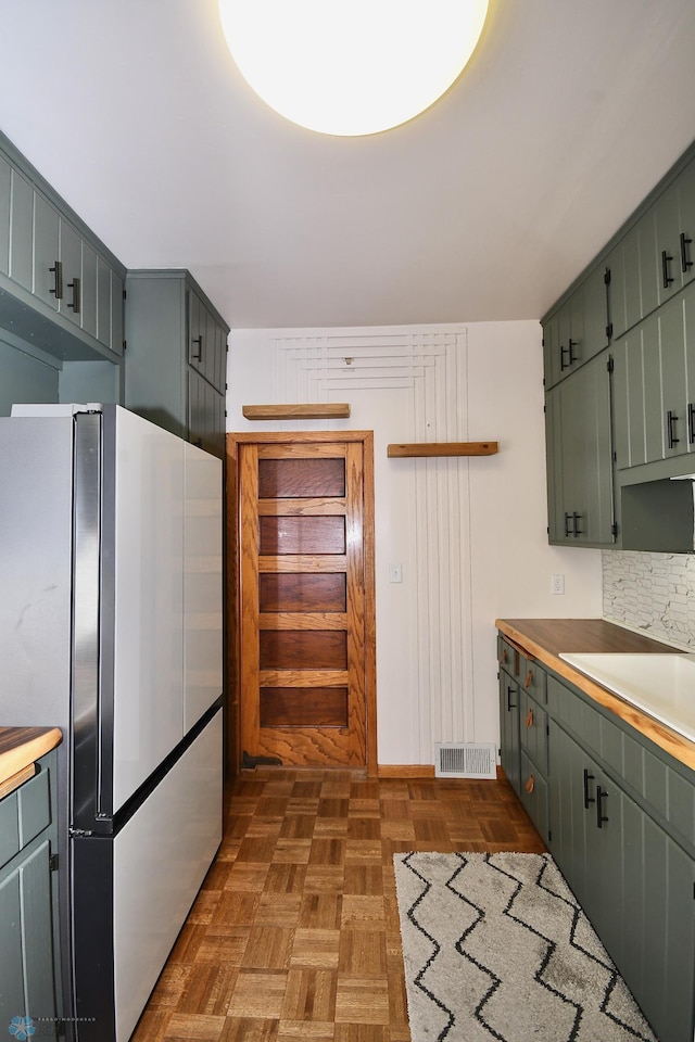 kitchen with dark parquet floors, stainless steel refrigerator, and tasteful backsplash