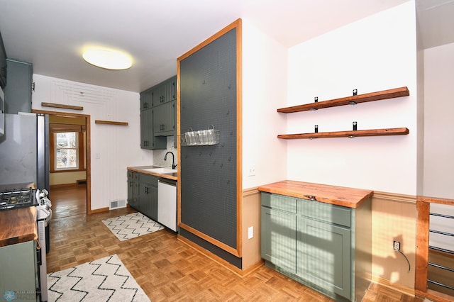 kitchen featuring stainless steel refrigerator, sink, parquet floors, dishwashing machine, and range