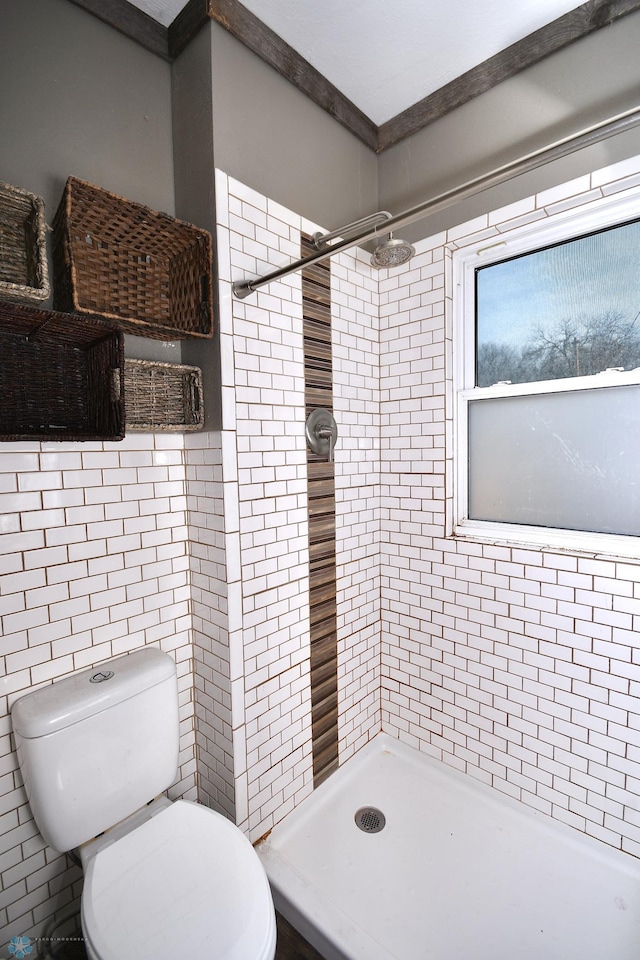 bathroom featuring tiled shower, toilet, and tile walls