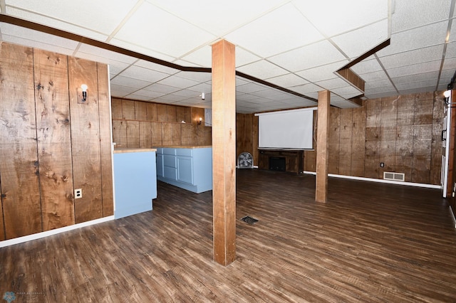 basement featuring a paneled ceiling, wood walls, and dark hardwood / wood-style flooring