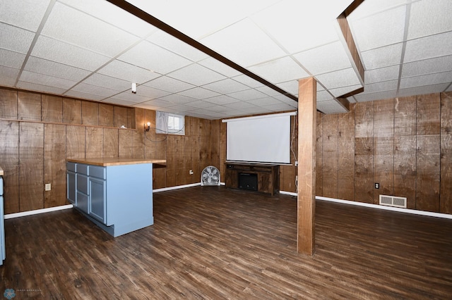 basement featuring a drop ceiling, dark hardwood / wood-style flooring, and wooden walls