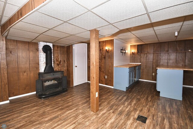 unfurnished living room featuring a paneled ceiling, dark hardwood / wood-style floors, wood walls, and a wood stove